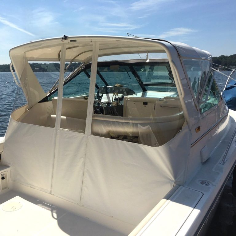 Boat cockpit with clear windshield, steering wheel, and docked boats in the background.